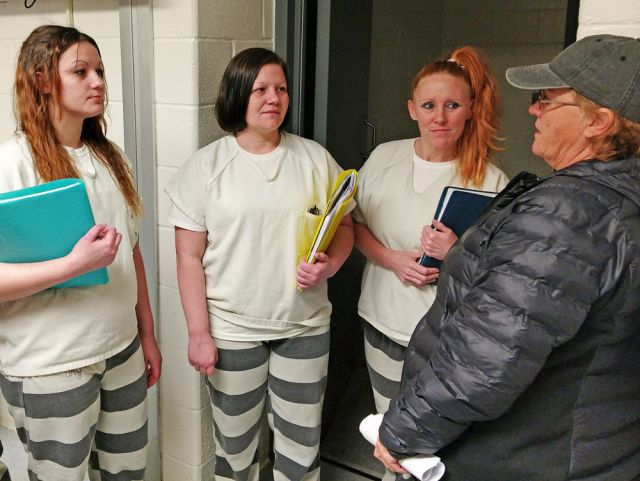 woman in hat talking to three female inmates with notebooks