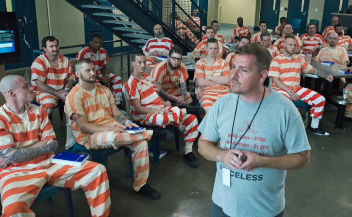 man speaking to group of inmates in striped uniforms